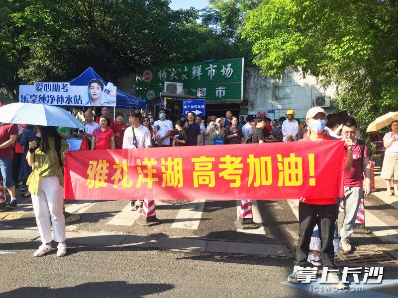 姜奕軒（右）和同學一起手舉著“雅禮洋湖 高考加油”的橫幅為考生打氣加油,。全媒體記者 劉俊 攝