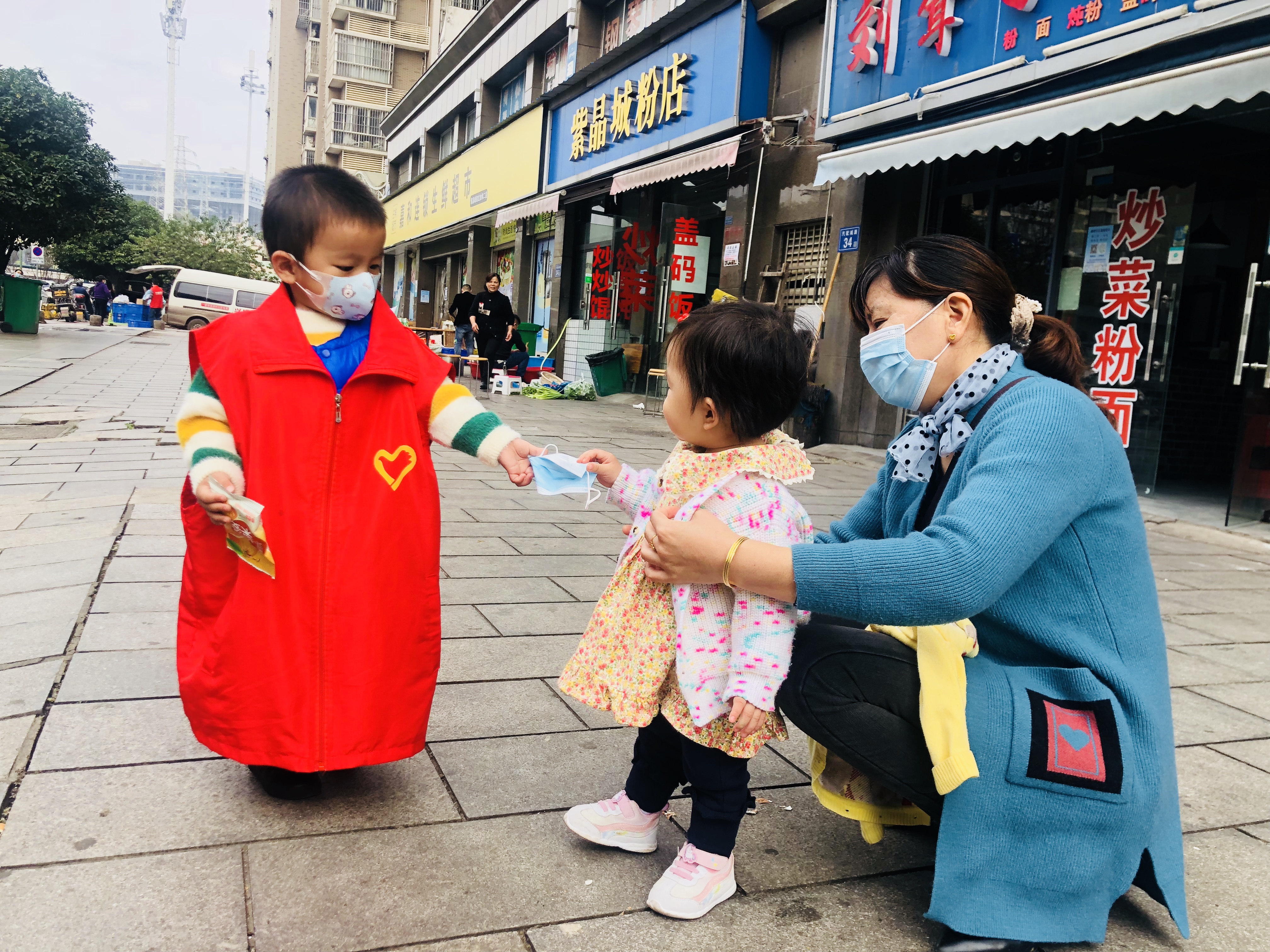 26日，跟著媽媽來“上班”,，3歲萌娃志愿者鄒涵睿給沒佩戴口罩的居民送口罩,。