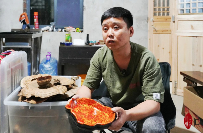 王鑫手捧著做好的大漆靈芝盤，在他的右手邊是還未進(jìn)行加工的靈芝,。